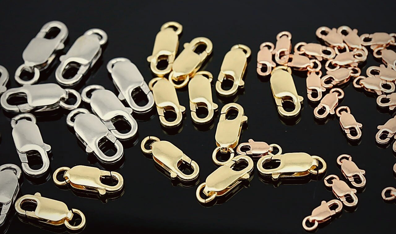 Rows of lobster clasps in silver, gold and rose gold finishes on a glossy black surface