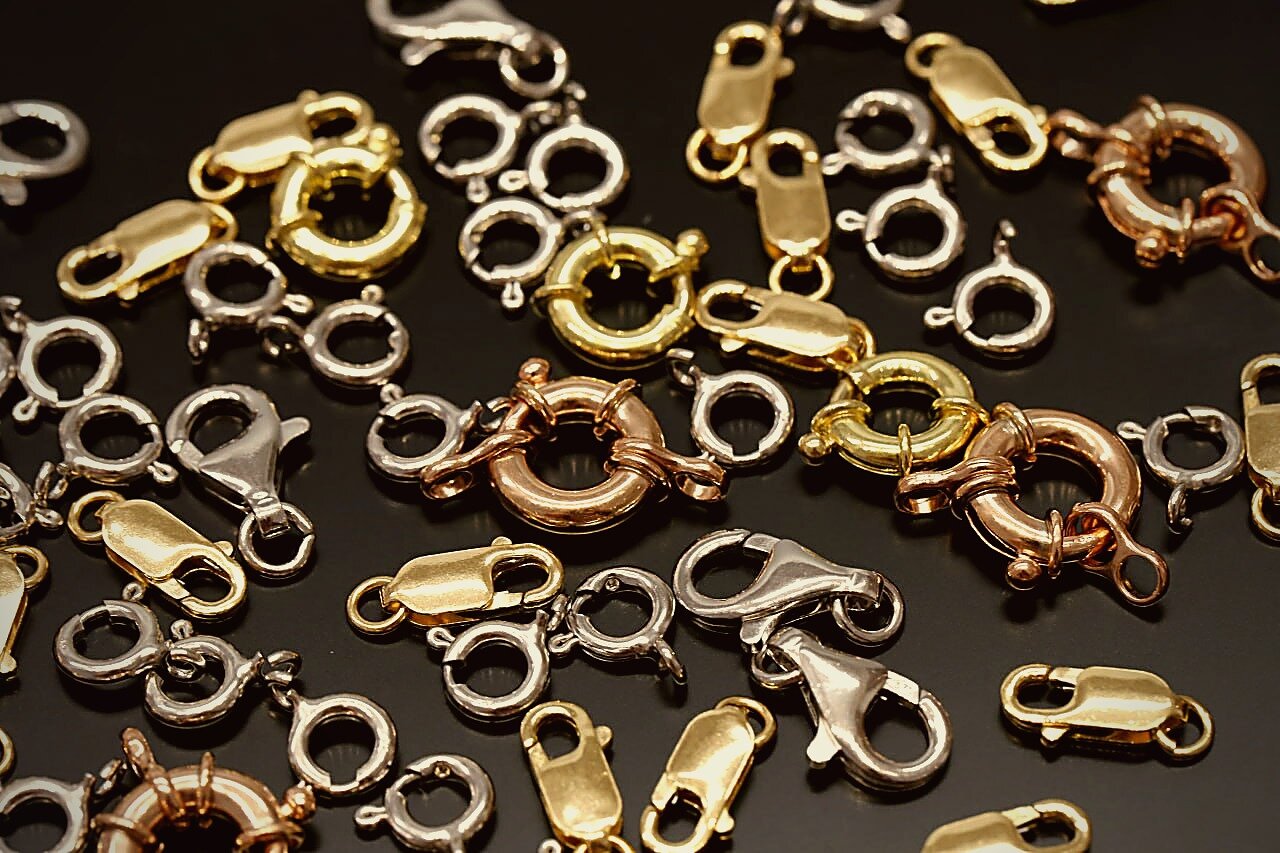 Assorted lobster, spring ring and toggle clasps in silver, gold and rose gold finishes on a dark reflective surface