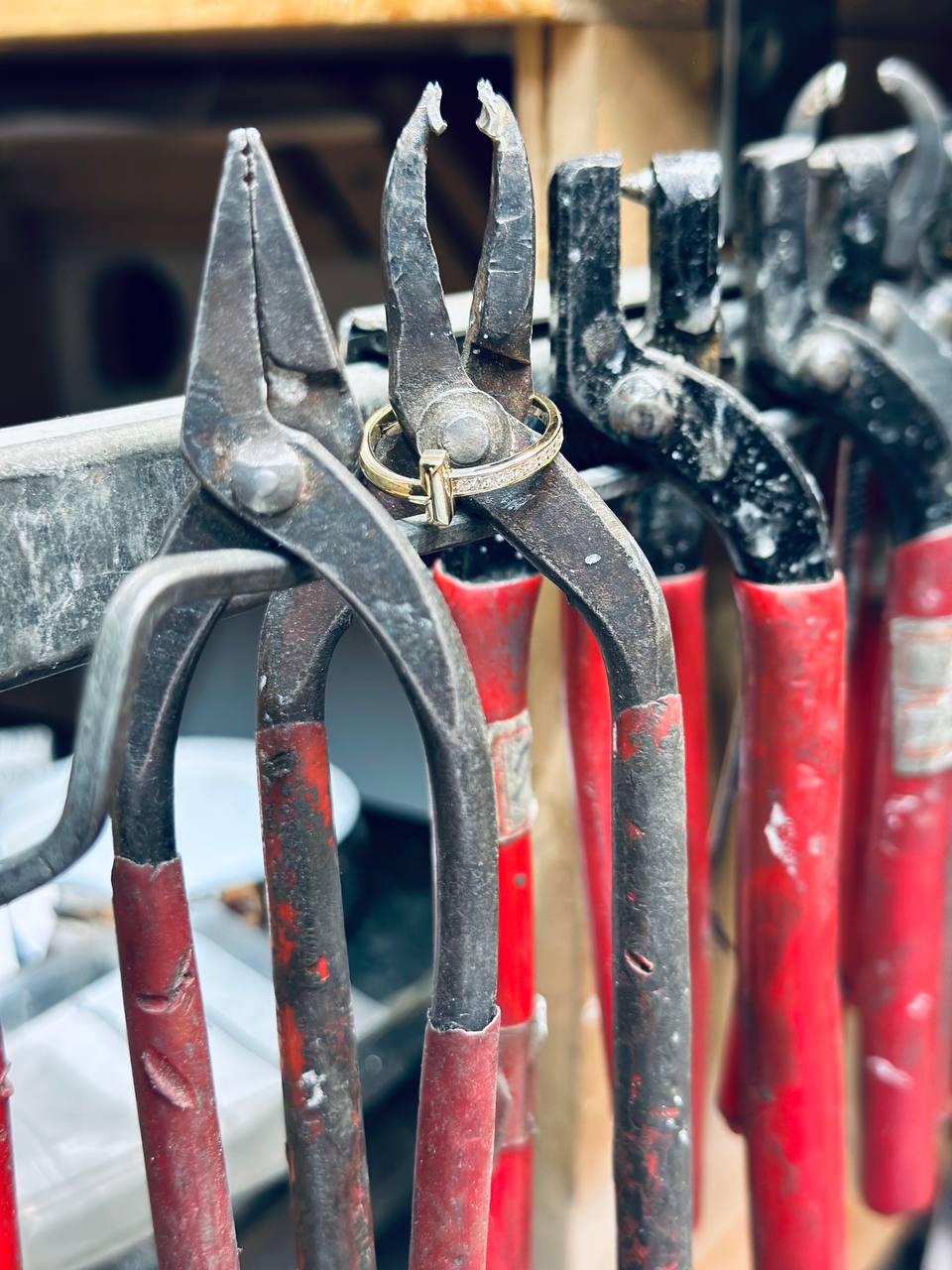 Worn bench pliers and nippers on the workshop rack, a gold ring resting on a tool pivot